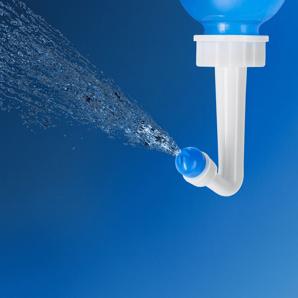 Demonstration des kräftigen Wasserstrahls, der aus dem Aufsatz der Nasenspülflasche kommt, vor dunkelblauem Hintergrund.