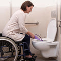 Frau im Rollstuhl benutzt die Urinierhilfe über der Toilette